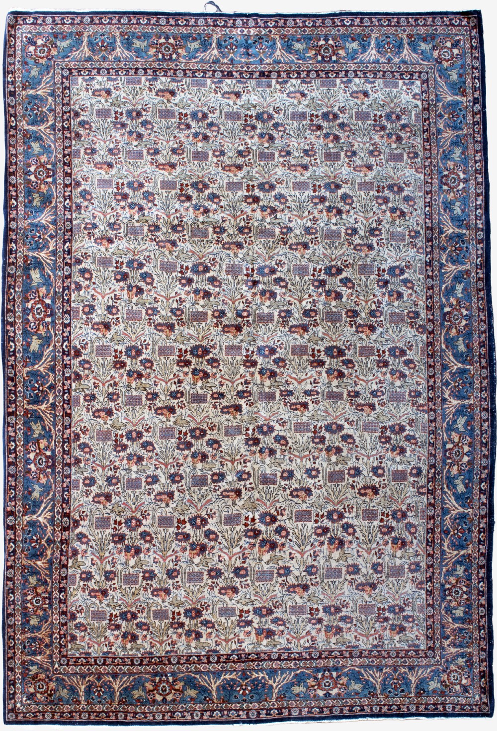A rectangular hand-knotted Persian Qum carpet featuring an intricate botanical pattern on a cream field framed by a dark blue patterned border.