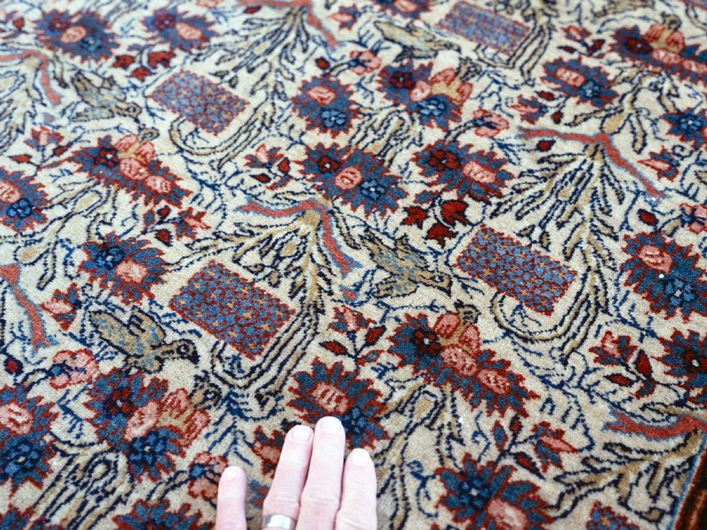 A rectangular hand-knotted Persian Qum carpet featuring an intricate botanical pattern on a cream field framed by a dark blue patterned border. View IV