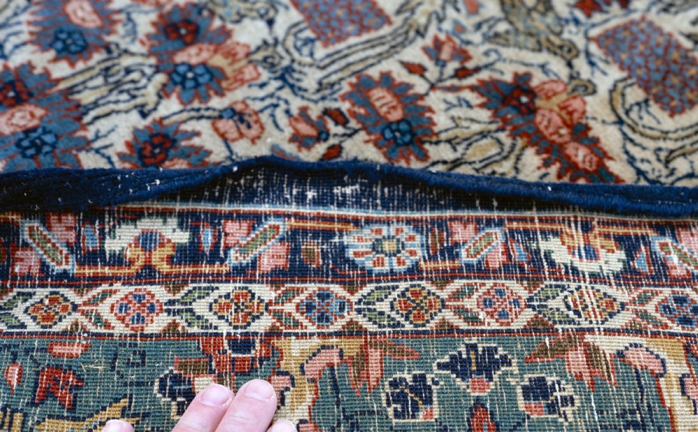 A rectangular hand-knotted Persian Qum carpet featuring an intricate botanical pattern on a cream field framed by a dark blue patterned border. View VI