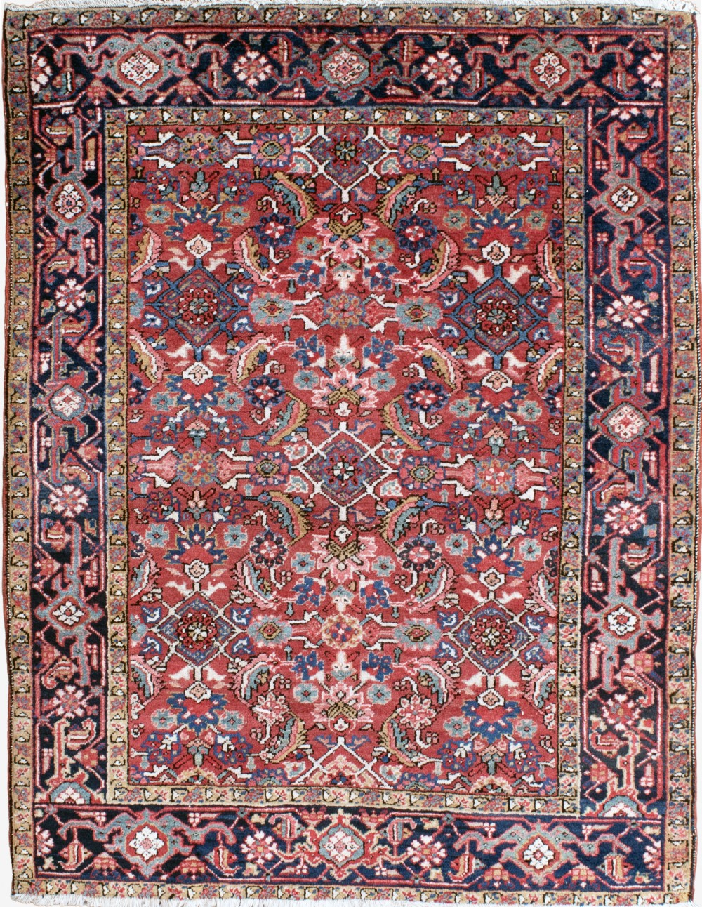 An antique Persian Heriz wool rug featuring a rich red field decorated with intricate geometric floral motifs framed by a dark navy blue patterned border.