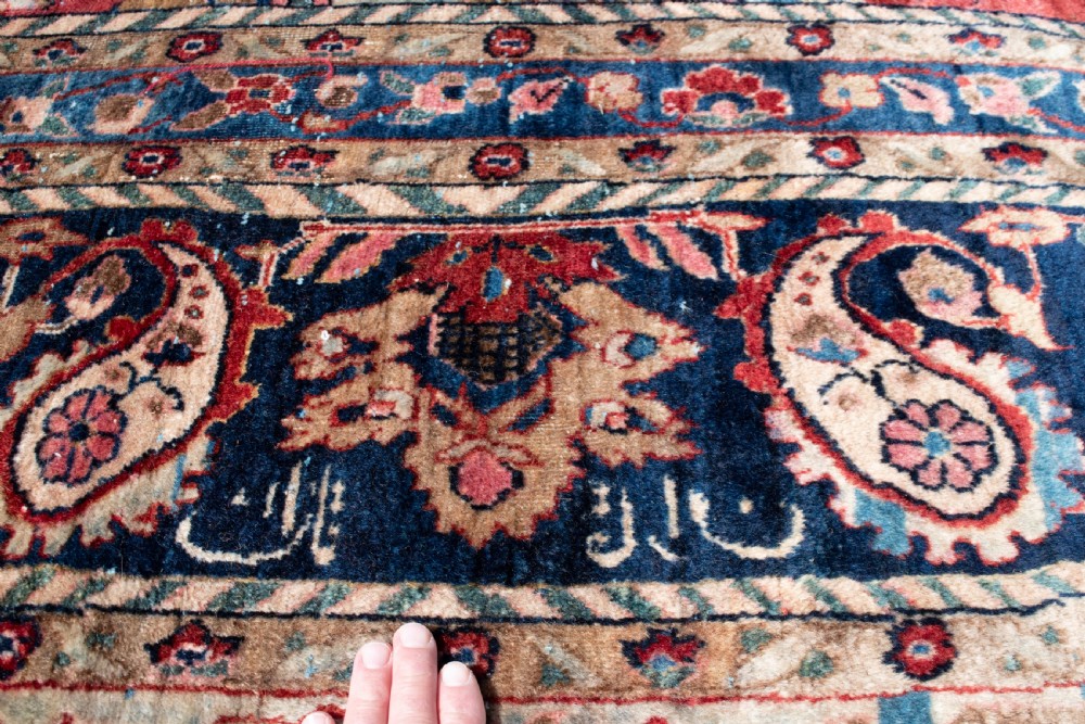 A large hand-knotted Persian Kashan carpet featuring a detailed red field covered in floral motifs framed by a multi-tiered navy blue border. View VI