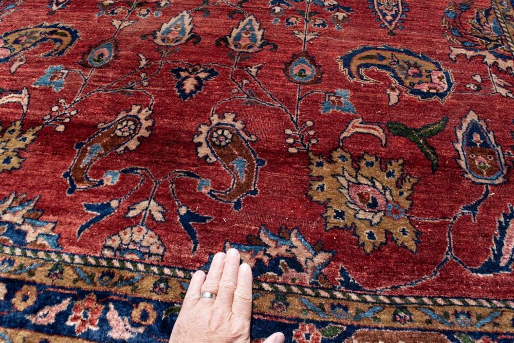 A large hand-knotted Persian Kashan carpet featuring a detailed red field covered in floral motifs framed by a multi-tiered navy blue border. View VII