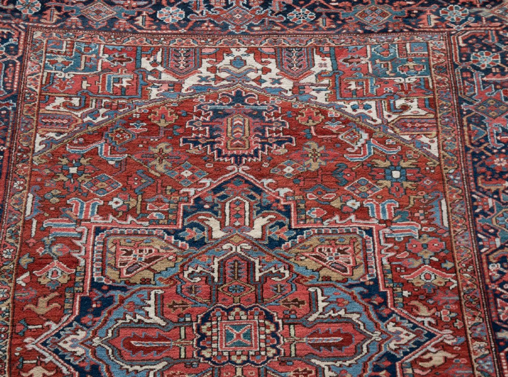 A large hand-knotted wool Heriz carpet featuring a central geometric medallion framed by intricate borders in shades of rust red, navy blue, and ivory. View II