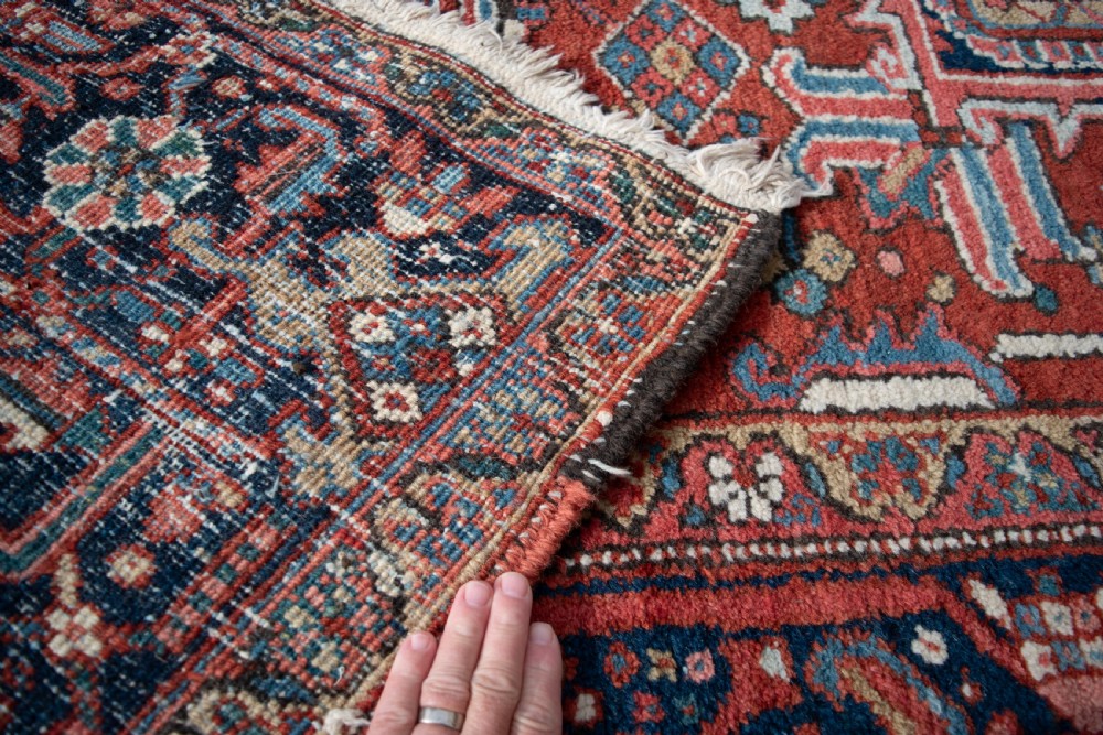 A large hand-knotted wool Heriz carpet featuring a central geometric medallion framed by intricate borders in shades of rust red, navy blue, and ivory. View IV
