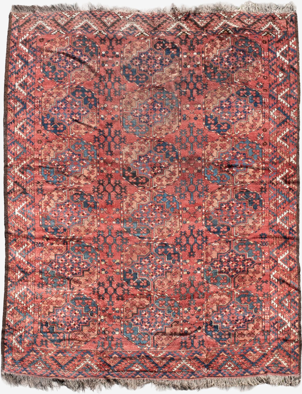 An antique hand-knotted Ersari wool carpet featuring repeating octagonal gul motifs in navy and ivory on a terracotta red field with geometric borders.
