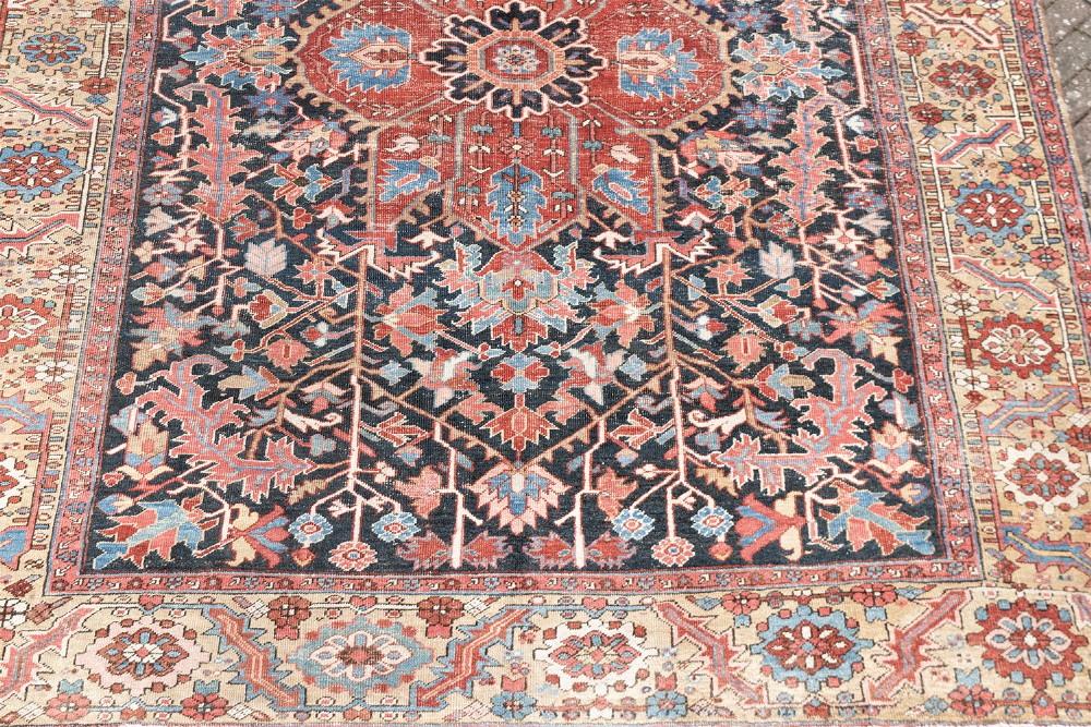 An antique Heriz wool carpet featuring a large red central geometric medallion on a dark navy blue field surrounded by an elaborate cream motif border. View III