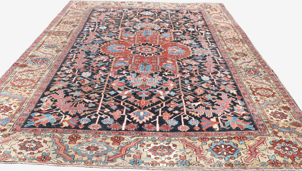 An antique Heriz wool carpet featuring a large red central geometric medallion on a dark navy blue field surrounded by an elaborate cream motif border. View IV