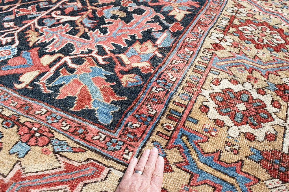An antique Heriz wool carpet featuring a large red central geometric medallion on a dark navy blue field surrounded by an elaborate cream motif border. View VI