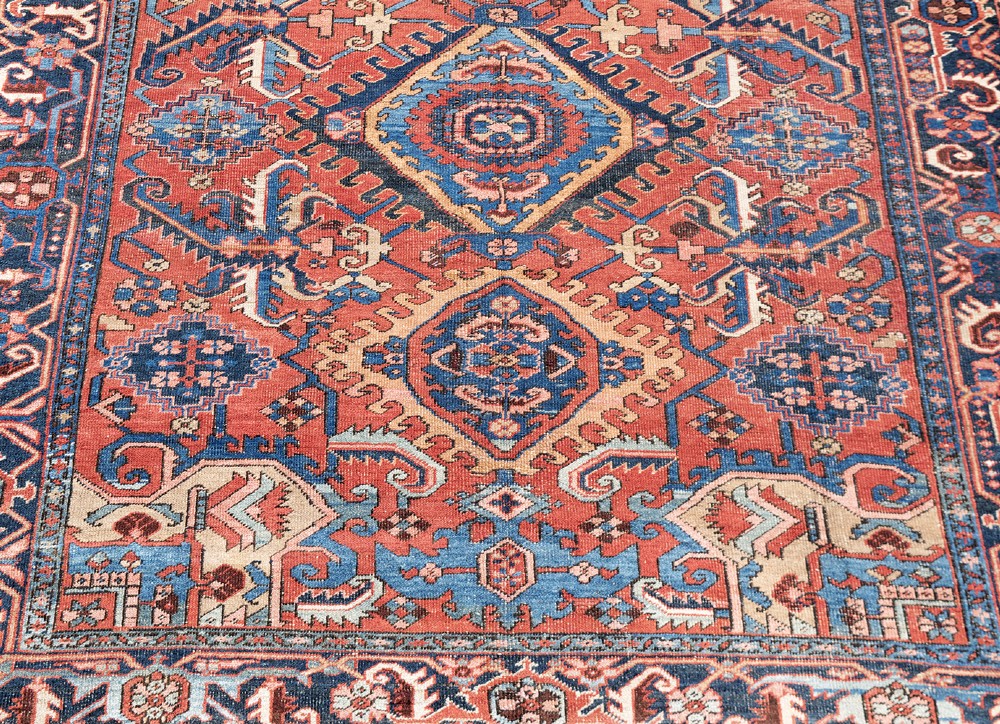 An antique Heriz wool carpet featuring a prominent geometric central medallion in blue and terracotta surrounded by angular botanical motifs and a patterned navy border. View II