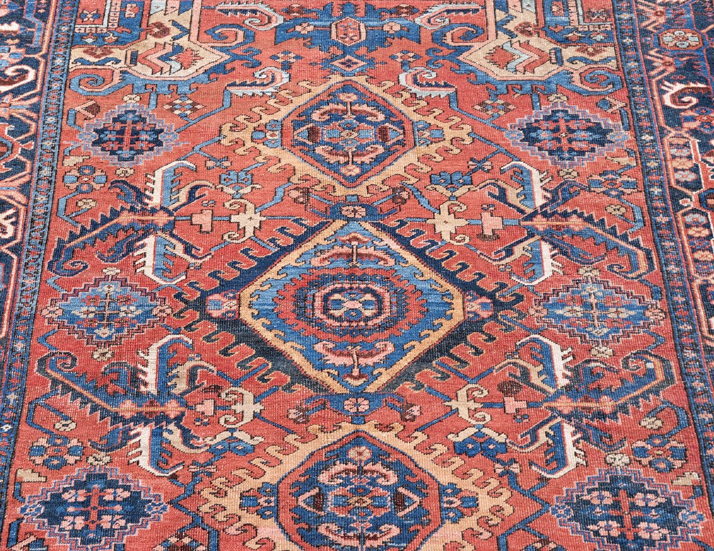An antique Heriz wool carpet featuring a prominent geometric central medallion in blue and terracotta surrounded by angular botanical motifs and a patterned navy border. View III