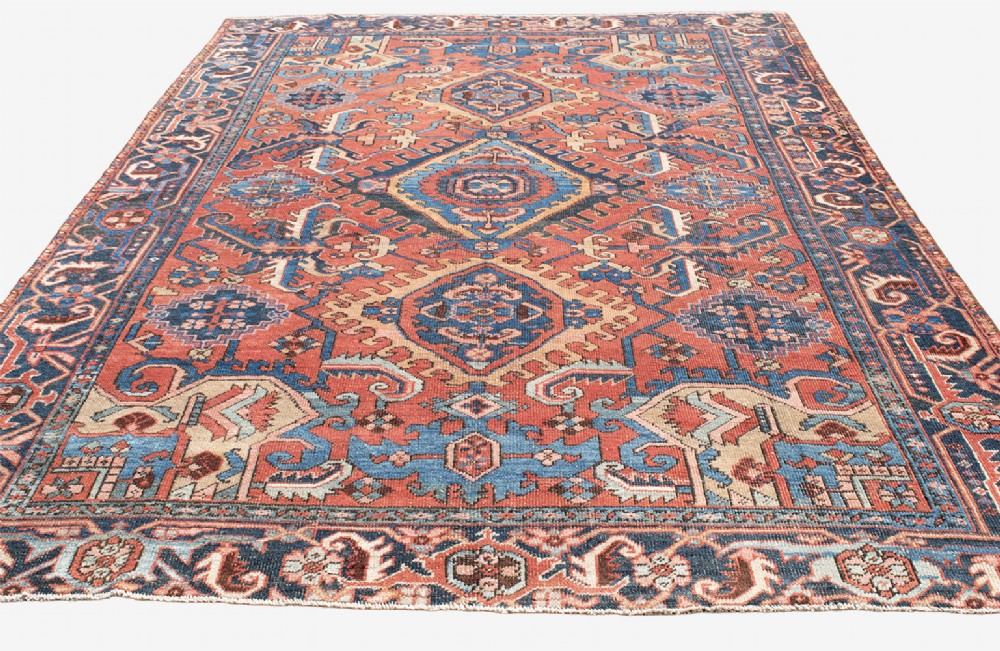 An antique Heriz wool carpet featuring a prominent geometric central medallion in blue and terracotta surrounded by angular botanical motifs and a patterned navy border. View IV