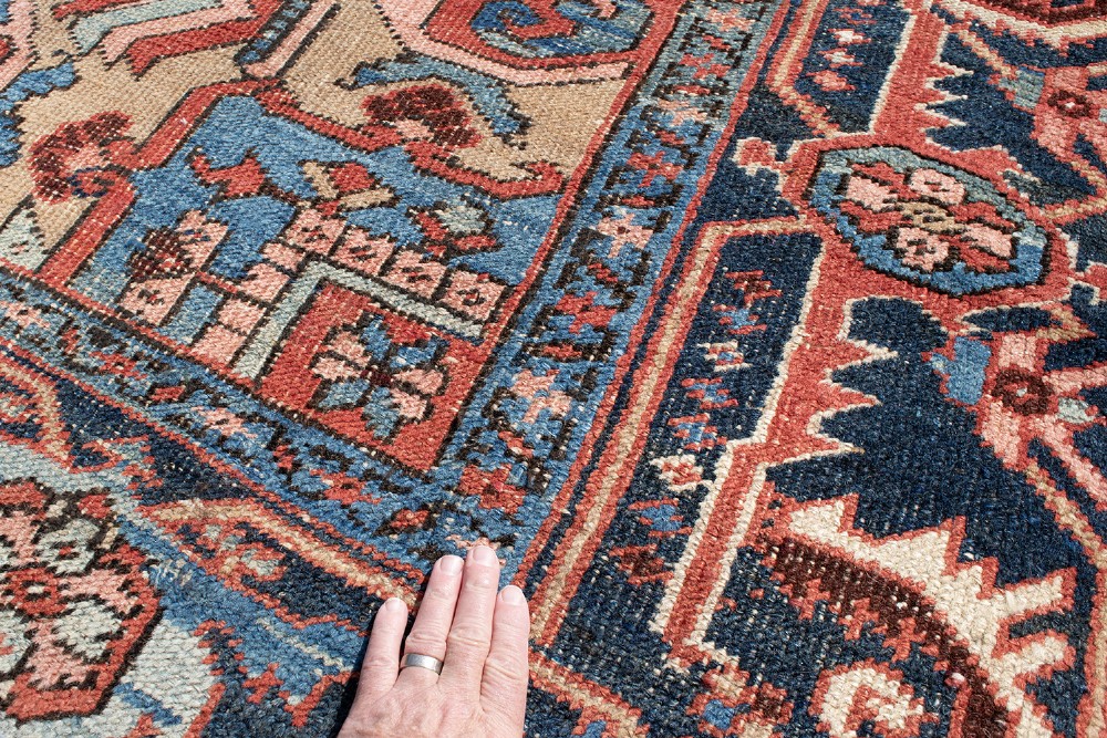 An antique Heriz wool carpet featuring a prominent geometric central medallion in blue and terracotta surrounded by angular botanical motifs and a patterned navy border. View VI