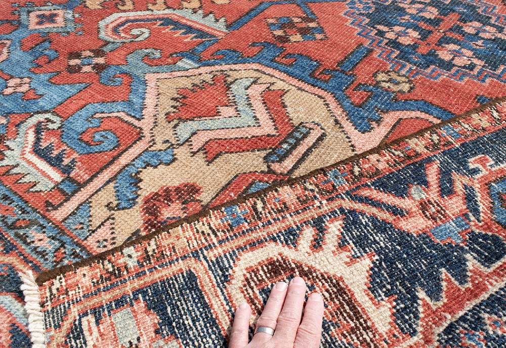 An antique Heriz wool carpet featuring a prominent geometric central medallion in blue and terracotta surrounded by angular botanical motifs and a patterned navy border. View VII