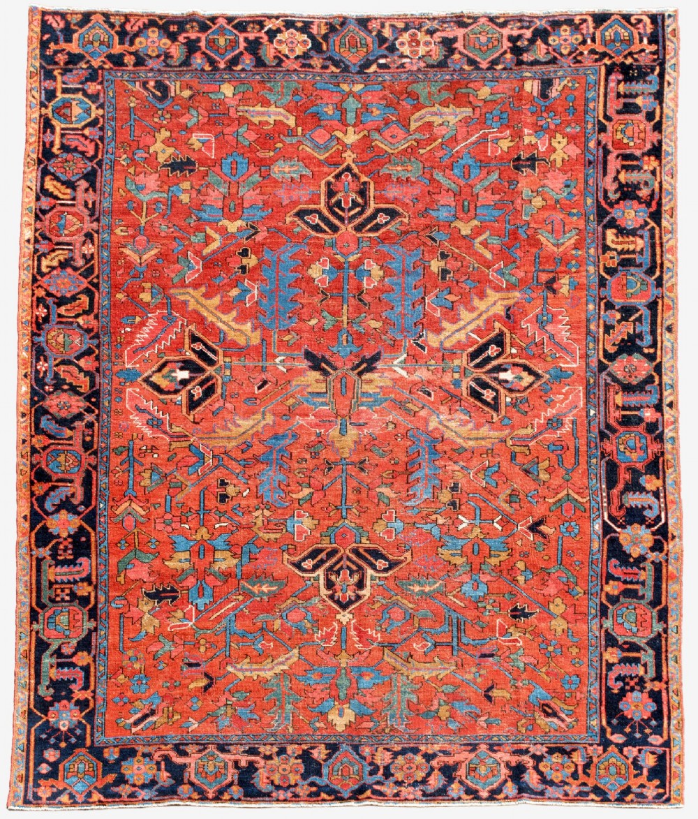 An antique Persian Heriz carpet featuring a central geometric medallion on a terracotta red field surrounded by navy blue borders.