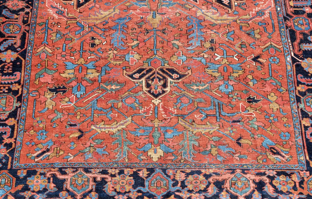 An antique Persian Heriz carpet featuring a central geometric medallion on a terracotta red field surrounded by navy blue borders. View II