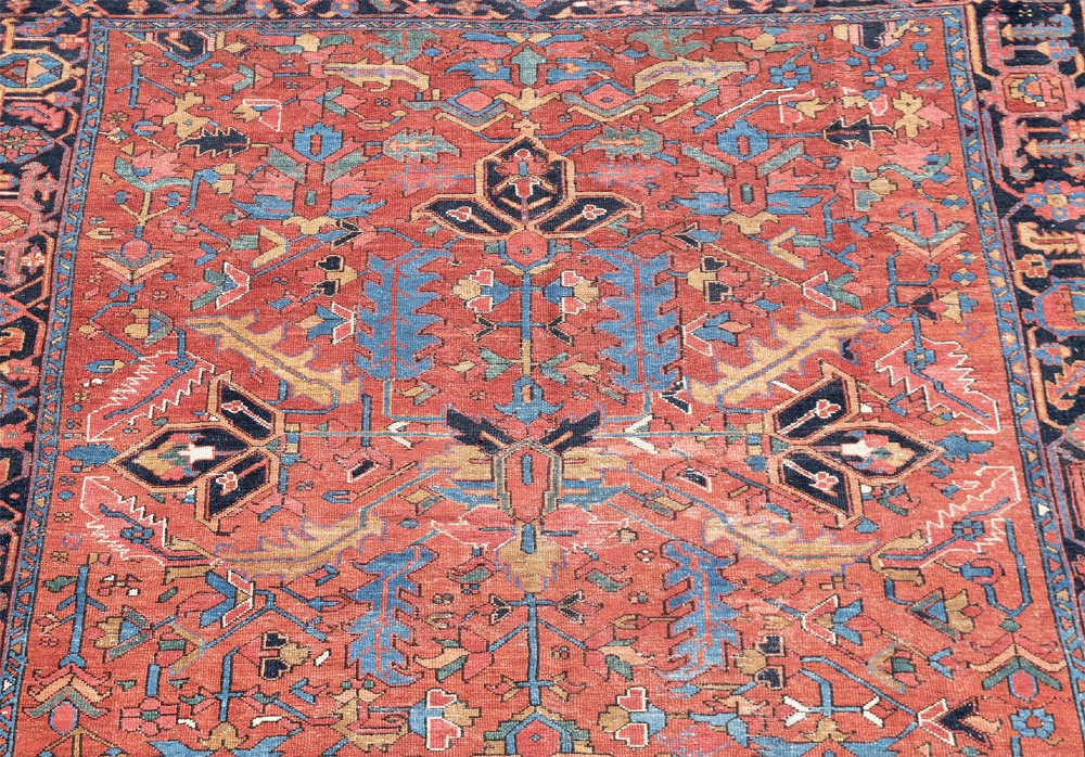 An antique Persian Heriz carpet featuring a central geometric medallion on a terracotta red field surrounded by navy blue borders. View III