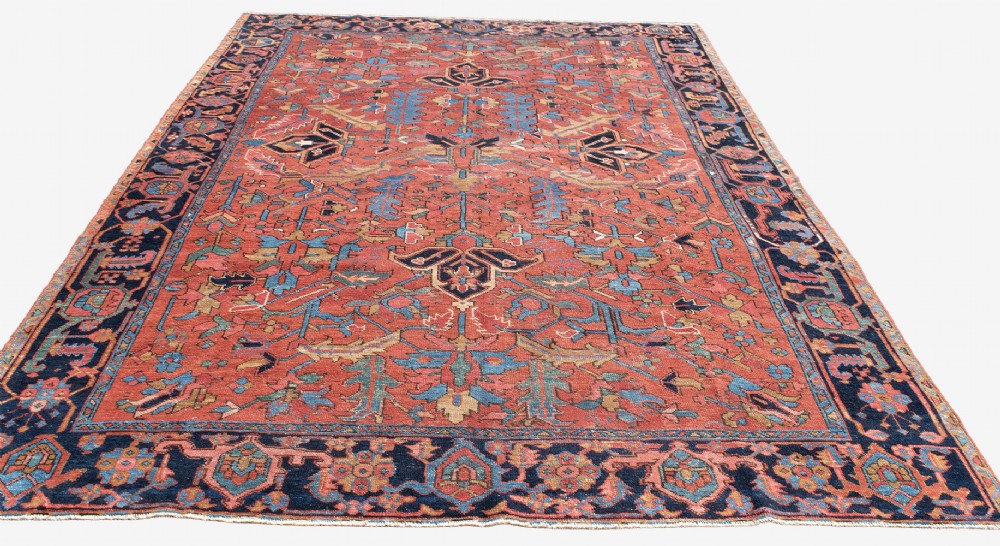 An antique Persian Heriz carpet featuring a central geometric medallion on a terracotta red field surrounded by navy blue borders. View V