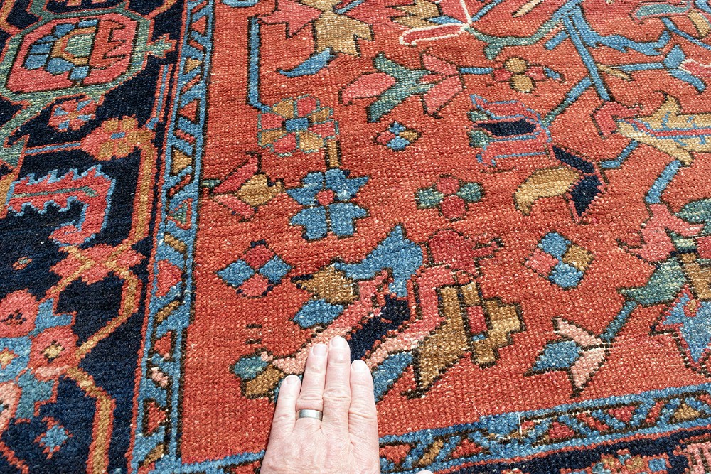 An antique Persian Heriz carpet featuring a central geometric medallion on a terracotta red field surrounded by navy blue borders. View VI