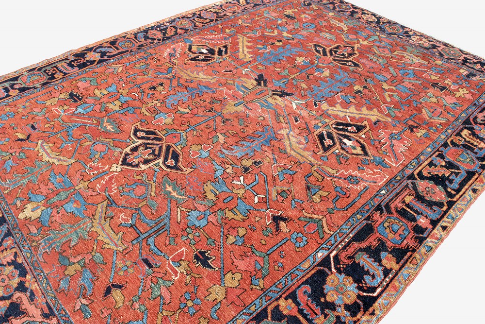 An antique Persian Heriz carpet featuring a central geometric medallion on a terracotta red field surrounded by navy blue borders. View VIII