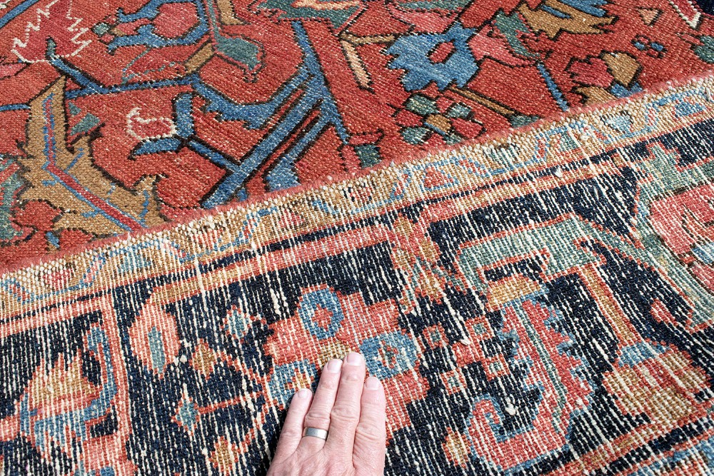 An antique Persian Heriz carpet featuring a central geometric medallion on a terracotta red field surrounded by navy blue borders. View IX