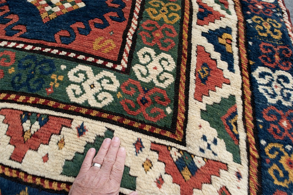 An antique Borchalu Kazak wool rug featuring stacked central diamond medallions surrounded by geometric borders in red, blue, green, and cream. View III