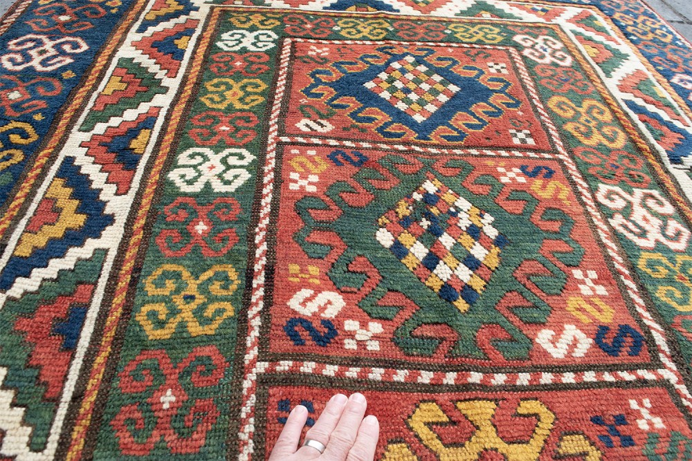 An antique Borchalu Kazak wool rug featuring stacked central diamond medallions surrounded by geometric borders in red, blue, green, and cream. View V
