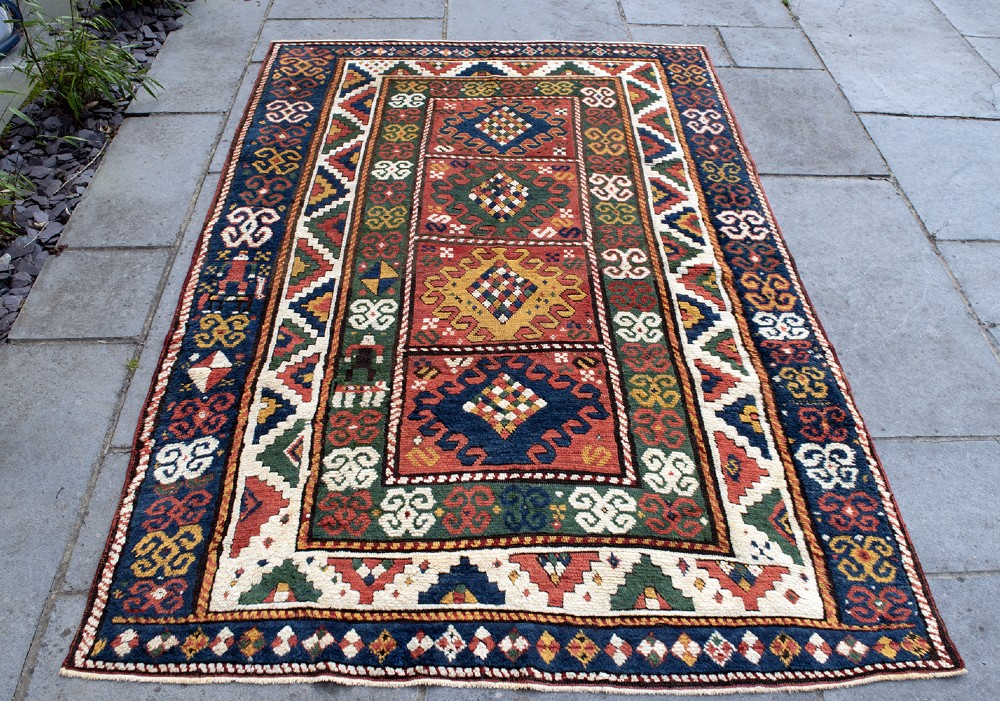 An antique Borchalu Kazak wool rug featuring stacked central diamond medallions surrounded by geometric borders in red, blue, green, and cream. View VIII