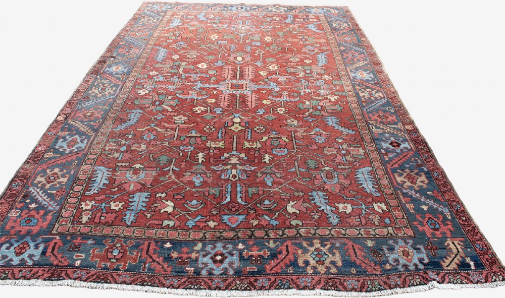 An antique hand-knotted Persian Heriz carpet featuring a terracotta red field with geometric motifs enclosed by a dark blue patterned border. View II