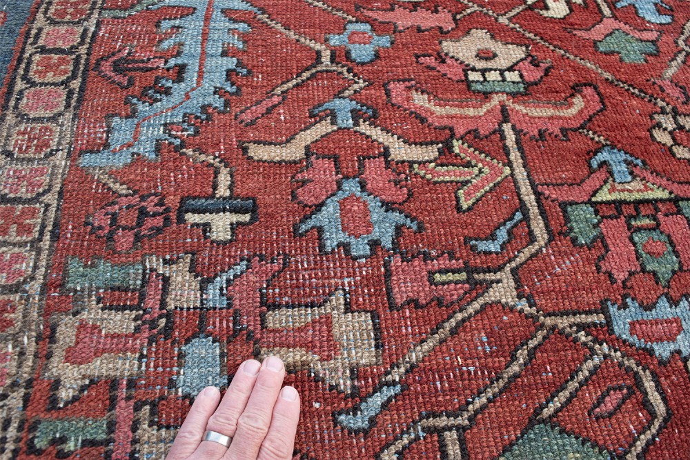 An antique hand-knotted Persian Heriz carpet featuring a terracotta red field with geometric motifs enclosed by a dark blue patterned border. View IV
