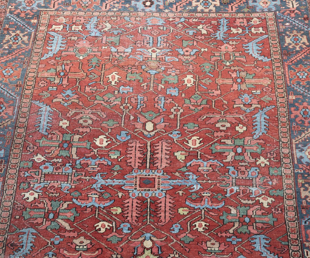 An antique hand-knotted Persian Heriz carpet featuring a terracotta red field with geometric motifs enclosed by a dark blue patterned border. View VII