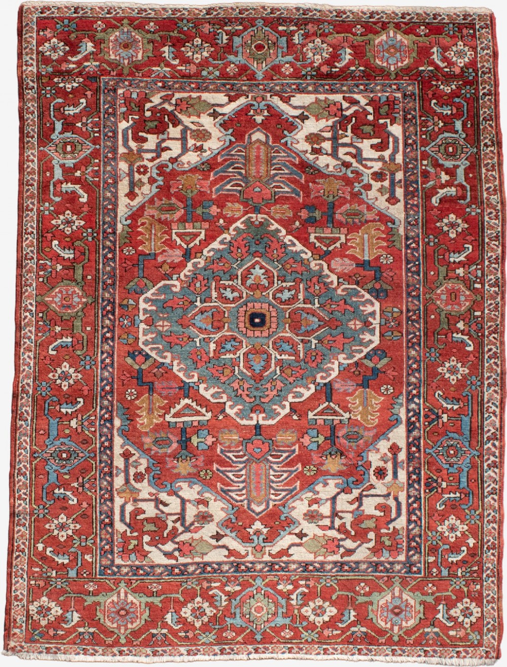 An antique Persian Serapi rug featuring a large central geometric diamond medallion in soft blue and terracotta on a red field with ivory spandrels.