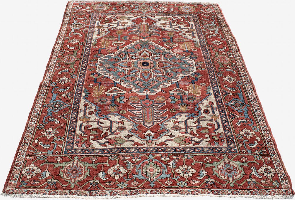 An antique Persian Serapi rug featuring a large central geometric diamond medallion in soft blue and terracotta on a red field with ivory spandrels. View III