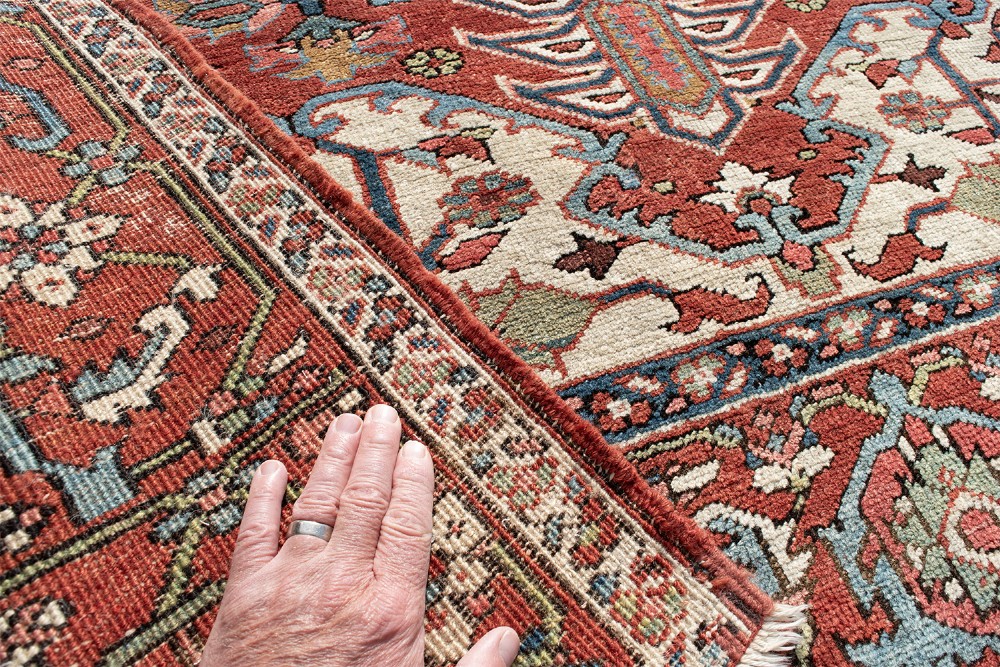 An antique Persian Serapi rug featuring a large central geometric diamond medallion in soft blue and terracotta on a red field with ivory spandrels. View VII