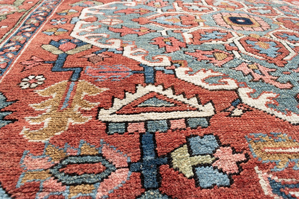 An antique Persian Serapi rug featuring a large central geometric diamond medallion in soft blue and terracotta on a red field with ivory spandrels. View VIII