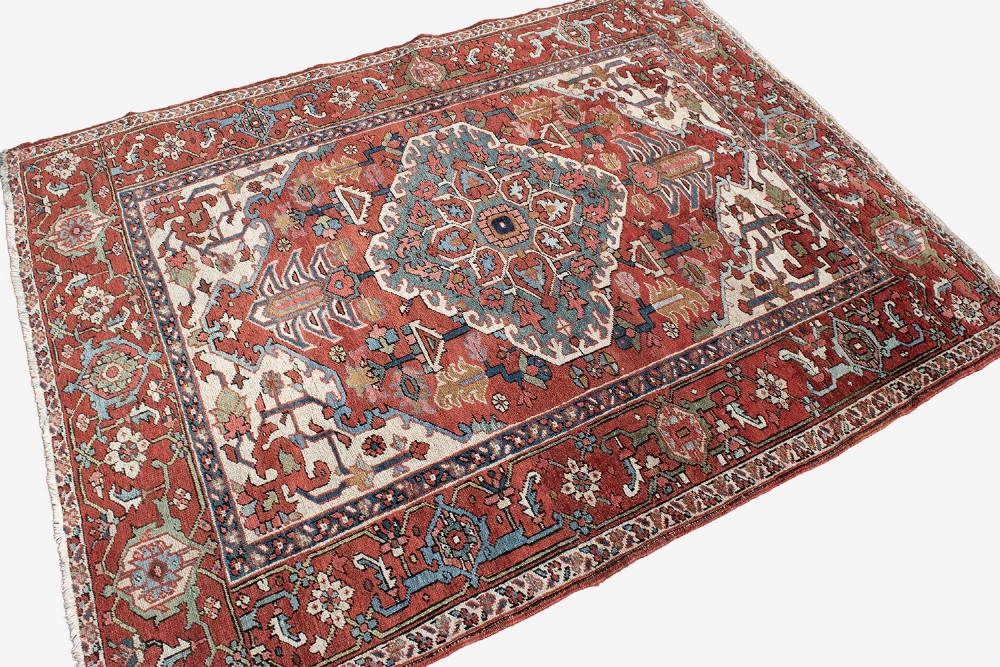 An antique Persian Serapi rug featuring a large central geometric diamond medallion in soft blue and terracotta on a red field with ivory spandrels. View X