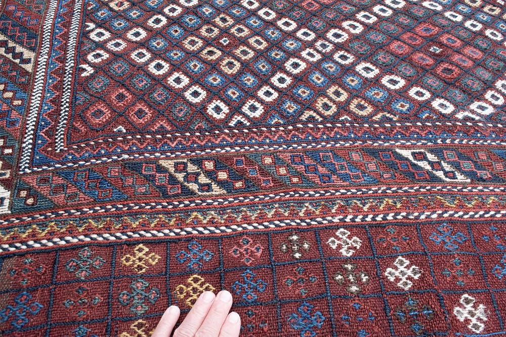 An antique Persian Afshar flatwoven Sofreh rug with a geometric diamond lattice pattern in crimson red, navy blue, and cream. View V
