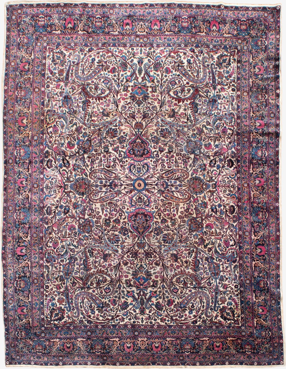 A large Kirman wool carpet featuring intricate floral scrollwork, paisley boteh motifs, and a central medallion in cream, magenta, and navy blue tones.