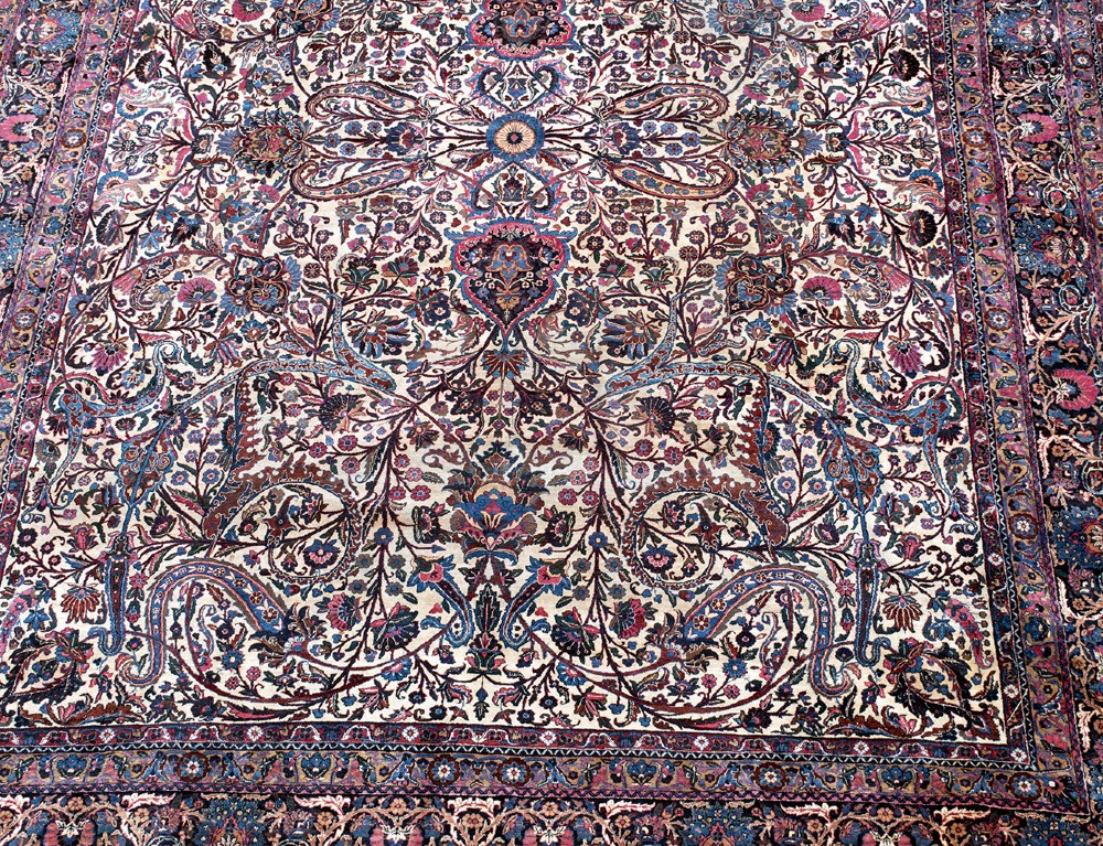 A large Kirman wool carpet featuring intricate floral scrollwork, paisley boteh motifs, and a central medallion in cream, magenta, and navy blue tones. View III