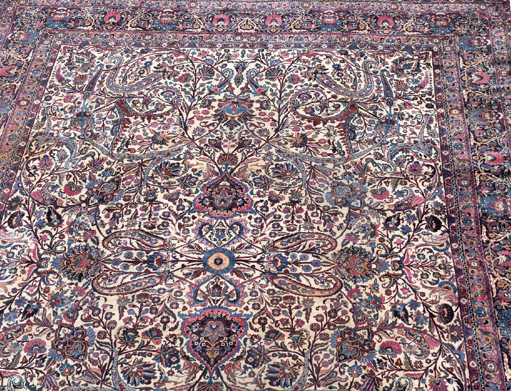 A large Kirman wool carpet featuring intricate floral scrollwork, paisley boteh motifs, and a central medallion in cream, magenta, and navy blue tones. View IV