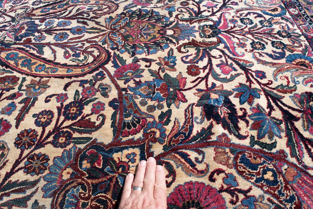 A large Kirman wool carpet featuring intricate floral scrollwork, paisley boteh motifs, and a central medallion in cream, magenta, and navy blue tones. View VI