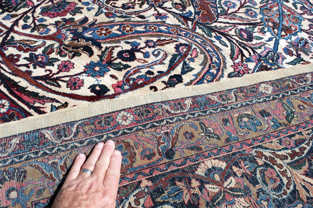 A large Kirman wool carpet featuring intricate floral scrollwork, paisley boteh motifs, and a central medallion in cream, magenta, and navy blue tones. View VII