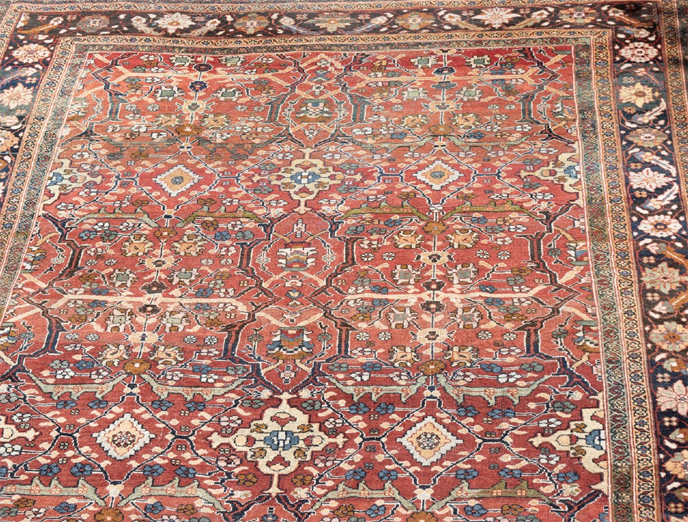 A large hand-knotted antique Persian Mahal carpet featuring a terracotta field filled with an intricate floral lattice pattern framed by a navy blue floral border. View IV