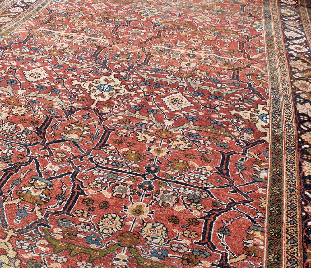 A large hand-knotted antique Persian Mahal carpet featuring a terracotta field filled with an intricate floral lattice pattern framed by a navy blue floral border. View VI