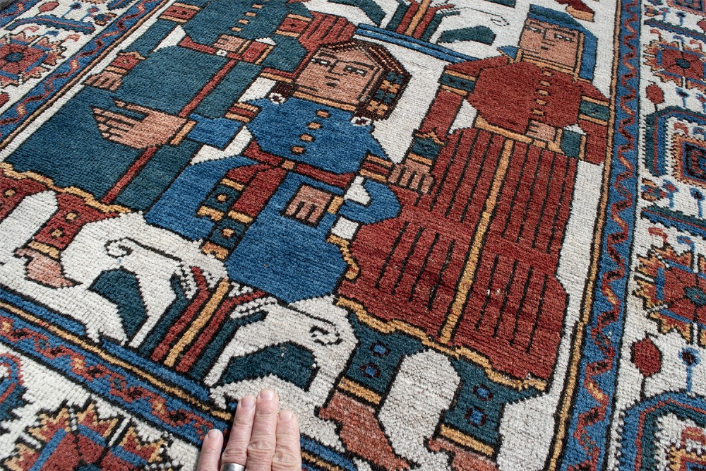 An antique Baluch pictorial wool rug featuring figurative human characters and a rider on horseback on a cream central field with geometric borders. View V