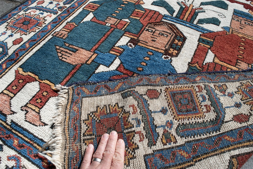 An antique Baluch pictorial wool rug featuring figurative human characters and a rider on horseback on a cream central field with geometric borders. View VI
