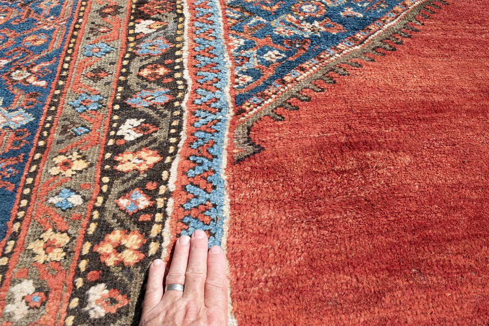 A large hand-knotted antique Ferahan wool carpet featuring a terracotta red field, a central diamond-shaped blue medallion, and detailed ornamental borders. View VI