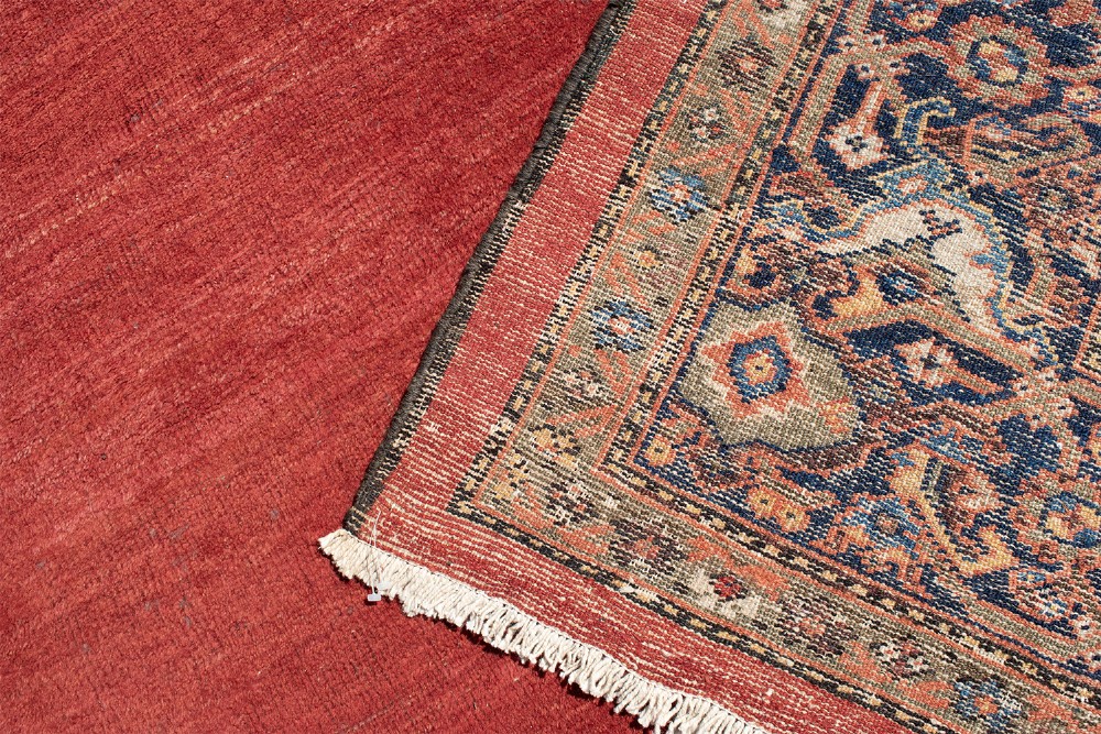 A large hand-knotted antique Ferahan wool carpet featuring a terracotta red field, a central diamond-shaped blue medallion, and detailed ornamental borders. View VII