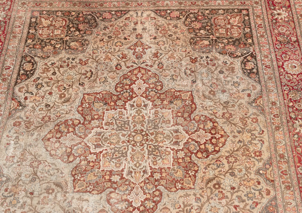 A large Persian Tabriz carpet featuring a central floral medallion on a cream field framed by deep red borders. View IV