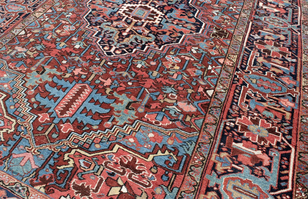 A hand-knotted Heriz wool rug featuring a central navy and ivory geometric medallion on a terracotta red field surrounded by intricate floral borders. View IV