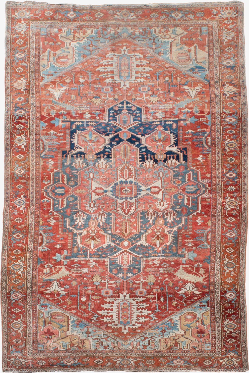 An antique Persian Heriz wool carpet featuring a bold geometric indigo medallion set against a terracotta red field with stepped spandrels and ornate borders.